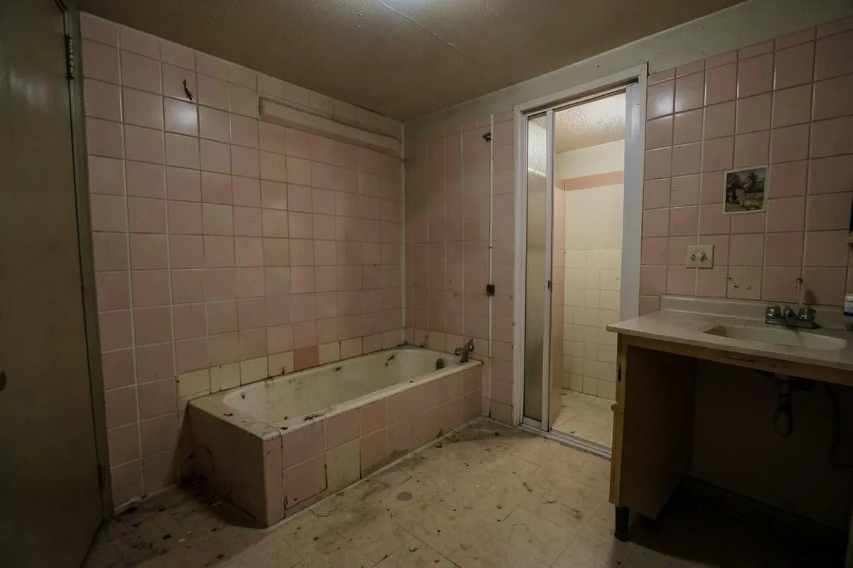 Dated bathroom with pink wall tile, an old alcove bathtub and a worn vinyl floor before renovation